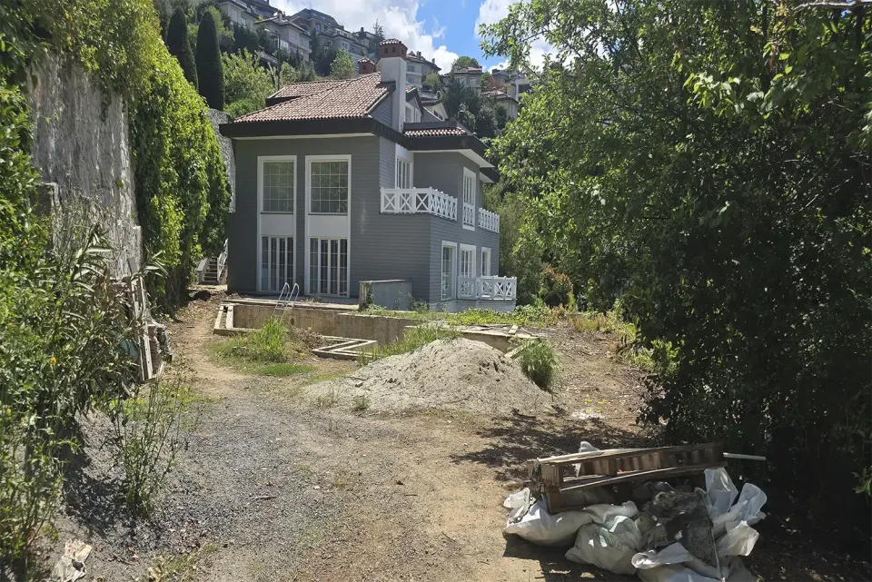 Bahçe yolundan görünen gri villa, kum yığını ve tadilat malzemeleri