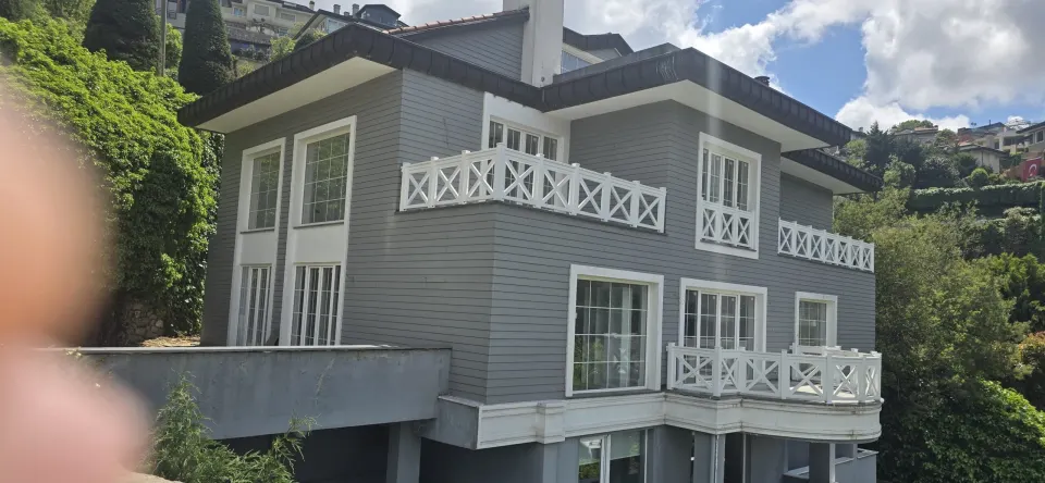 Yeşil yamaçtaki gri ahşap kaplama villada beyaz çapraz korkuluklu geniş balkonlar