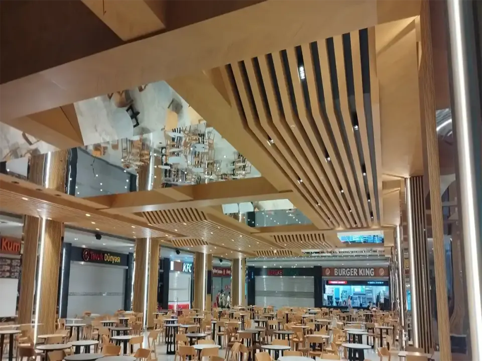 Açılı ahşap çıta kirişlerin aynalı panelle buluştuğu yemek alanı ve arkadaki yiyecek tezgahları
