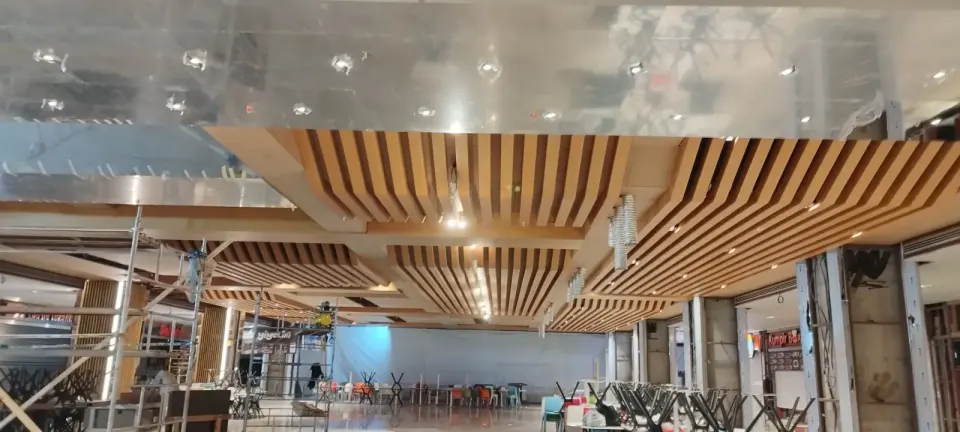 Şantiye halindeki yemek alanında çıtalı tavan modülleri ve üstte parlak metal yüzey