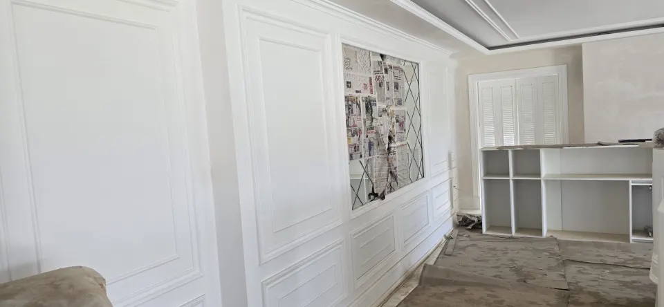 Villada beyaz boiserie duvar panelleri arasında korunan ayna ve açık raflı beyaz ünite