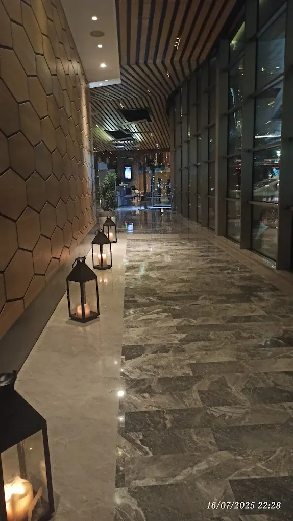 Otel resepsiyonuna uzanan koridorda altıgen duvar kaplaması, mermer zemin ve fenerler